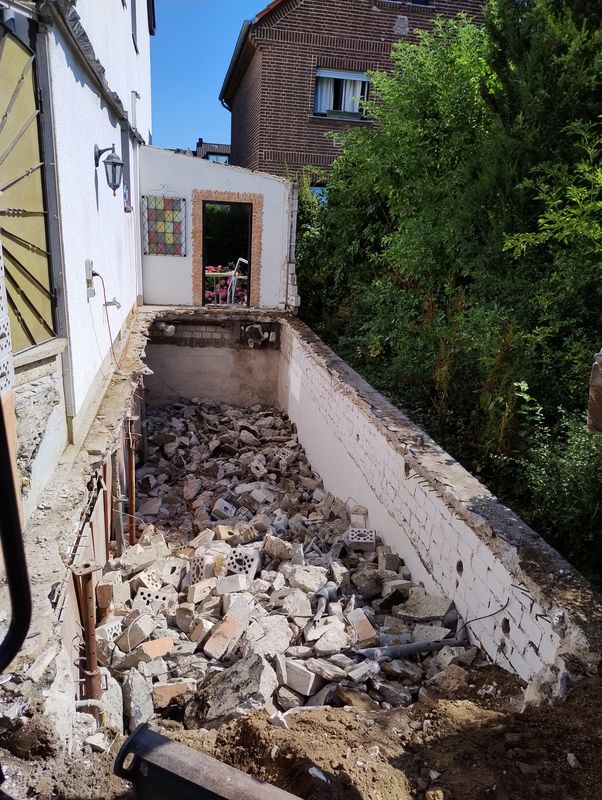Abbrucharbeiten in einem schmalen Gang zwischen Hauswand und Hecke