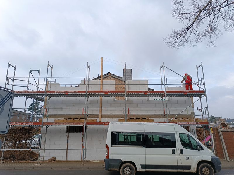 Eingerüsteter Anbau an einem Wohnhaus, davor der Firmentransporter