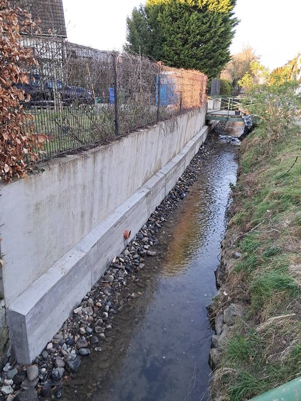 Unterfangene Stützwand aus Beton entlang eines Bachlaufs