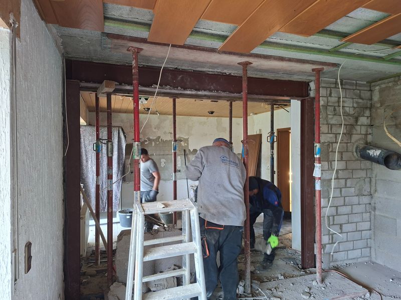 Wanddurchbruch in einem Einfamilienhaus: eingebauter Stahlträger, die Decke ist mit Baustützen abgefangen, Mitarbeiter bei der Arbeit